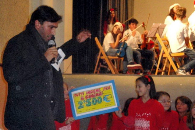I bambini cosegnano un assegno simbolico al vice-parroco don Matteo Monge per l'ammodernamento del cinema parrocchiale durante il Concerto di Natale